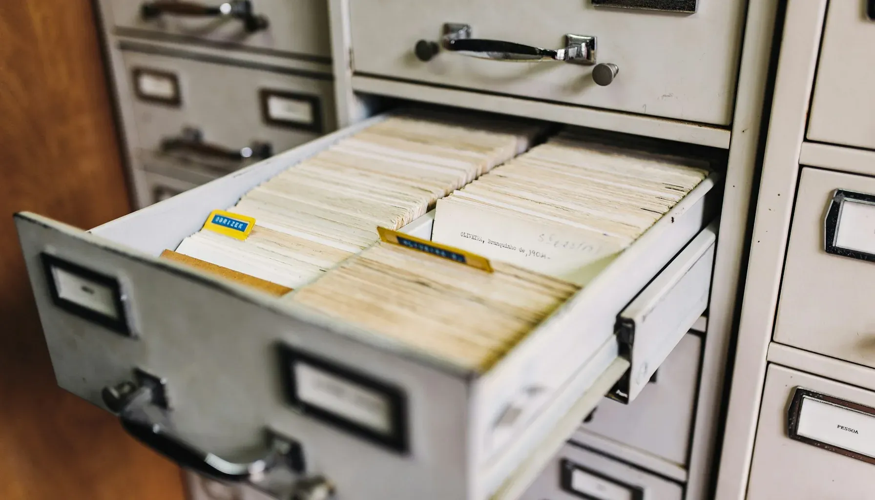 Photograph of a metal filing cabinet with one drawer pulled open, packed with densely filed index cards